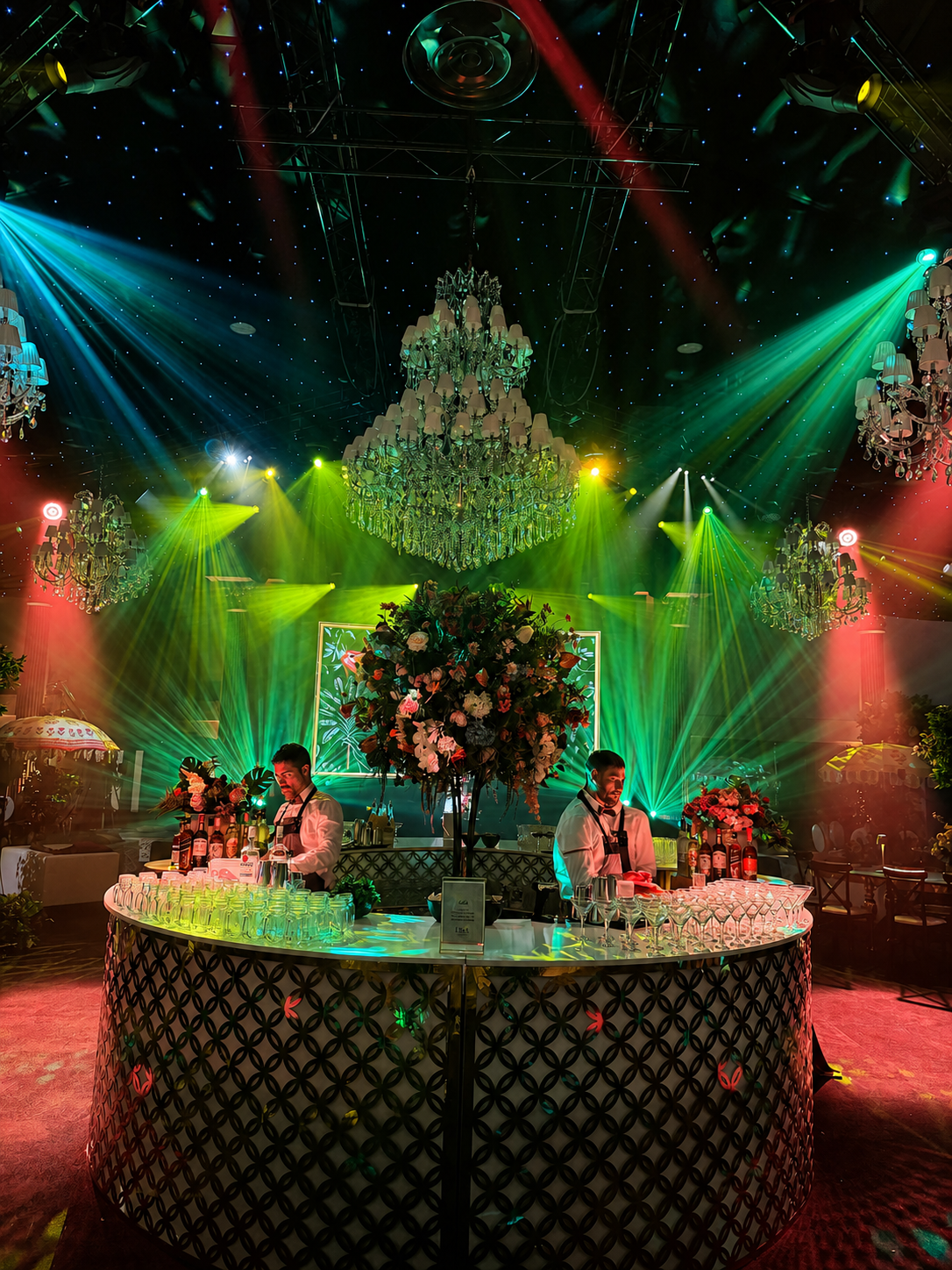 Colourful event lighting design illuminating chandeliers, a floral bar and star-cloth ceiling